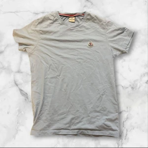 Ljusblå t-shirt från Moncler - Säljer en ljusblå t-shirt från Moncler med klassisk rund hals och korta ärmar. T-shirten har en liten broderad Moncler-logga på bröstet och är tillverkad i mjuk bomull. Perfekt för dig som gillar stilrena och enkla plagg med exklusiv touch.