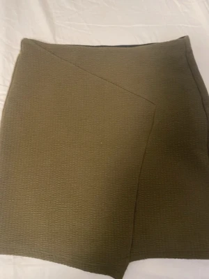 Olivgröna omlott skorts från Bershka XS - Snygga olivgröna skorts från Bershka i storlek XS. De har en omlott-design framtill och är gjorda i ett strukturerat syntetmaterial som ger en cool textur. 