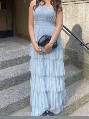 Ljusblå långklänning med volanger - Superfin ljusblå balklänning från ASOS med flera lager volanger och ett axelbandslöst, oneshoulder-snitts. Klänningen är använd 1 gång så väldigt fint skick! Skriv om du har funderingar 🩵🩵🩵🩵