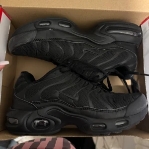 Svarta Nike Air Max sneakers - Säljer ett par helsvarta Nike Air Max sneakers med snygg vågig design och synliga luftkuddar i sulan. Skorna har mesh och syntetmaterial, rund tå och snörning. Perfekta för dig som gillar sportig och clean stil.