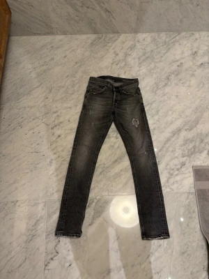 Svarta  jeans från dondup , storlek 29 - Säljer ett par svarta skinny jeans från dondup i storlek 29. Jeansen har en snygg tvättad look med slitning på ena benet och klassiska fem fickor. Passformen är tight och midjan är normal. Perfekta för dig som gillar en smal siluett och streetstil.