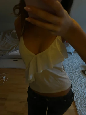 Vit linnetopp med volang  - Säljer en söt vit linnetopp från H&M i storlek XS. Toppen har smala ändringsbara axelband och en snygg volang framtill som ger en feminin touch. Materialet är lätt och skönt, perfekt för varma dagar. Passformen är normal och toppen är ärmlös.