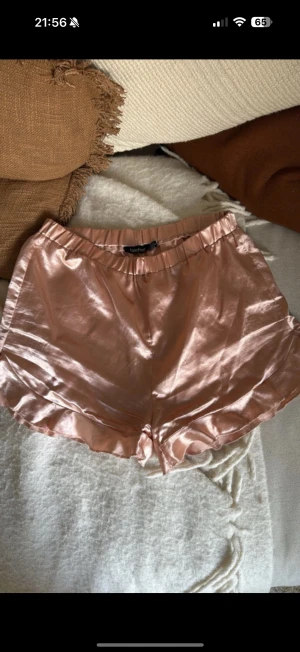 Champagnefärgade satinshorts Boohoo - Snygga champagnefärgade shorts från Boohoo i glansigt satinmaterial. Modellen är loose fit med elastisk midja och mjuka volangdetaljer längs bensluten. Perfekt för dig som gillar en chill och trendig vibe. Strl 38 sitter som 36