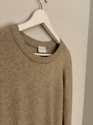 Beige stickad tröja från VILA - En enkel och snygg beige stickad tröja från VILA med rund hals och ribbade muddar vid ärmslut och nederkant. Perfekt att slänga på sig när det är lite kyligt ute. Långärmad och i mjukt material som känns skönt mot huden. Passar från 155 till 164!