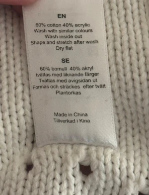 Vit omlottkofta från Bondelid - Säljer en vit stickad omlottkofta från Bondelid i storlek S. Koftan har långa ärmar, ribbade muddar och ett snyggt knytband i midjan. Detaljerad med små hålmönster och broderad Bondelid-logga framtill. Perfekt för lager-på-lager under kyliga dagar.