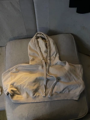 Beige croppad hoodie från Bik Bok - Snygg beige croppad hoodie från Bik Bok i storlek XS. Tröjan har huva med snörning och långa ärmar. Perfekt för dig som gillar en chill och trendig stil. Mjuk bomullskvalitet och ribbad kant nedtill ger en skön passform.storleken är xs-s skulle jag säga 