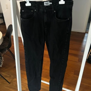 Svarta jeans från 157 New Classic - Svarta jeans från 157 New Classic med klassisk femficksdesign och raka ben. Jeansen har knapp och dragkedja i midjan samt bälteshällor. Materialet är robust denim och färgen är mörkt svart, perfekt för en clean och stilren look. Färgen har lossat lite