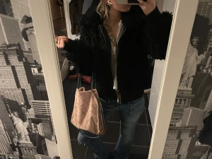 Svart teddyjacka - Säljer en svart teddyjacka med fluffig och krullig yta, croppad passform och långa ärmar. Jackan har en silverfärgad dragkedja framtill och ribbade muddar vid ärmslut och nederkant. Perfekt för dig som gillar en chill och trendig look.