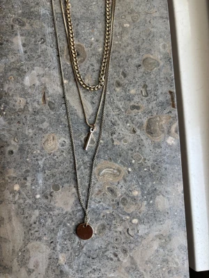 Layered halsband i silverfärg - Snyggt halsband med tre lager i silverfärg. Ena kedjan är grov och chunky, de andra två är tunnare med minimalistiska hängen – ett runt mynt och ett avlångt stavformat. Perfekt för dig som gillar att mixa olika stilar och skapa ett coolt statement.