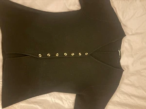 Svart kofta med kort ärm från Gina  - Svart kofta från Gina med korta ärmar. Tröjan har en stilren, rak passform och är gjord i mjukt material som känns lyxigt mot huden. Perfekt för dig som gillar minimalistisk och clean stil. Använd ett fåtal gånger