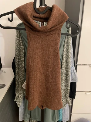 Brun stickad krage/huva - Säljer en brun stickad krage/huva i mjukt material. Perfekt att dra över huvudet för extra värme under jackan. Den har en hög polokrage och är i en enkel, stilren design utan detaljer. Passar perfekt för kalla dagar.