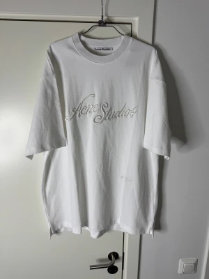 Vit Acne Studios t-shirt med 3d brodyr logga storlek M - Vit t-shirt från Acne Studios med broderad logga framtill i ton-i-ton. Oversized passform, rund halsringning och korta ärmar. Tillverkad i mjuk bomull för en clean och stilren look.