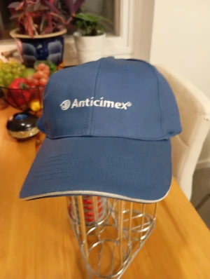 Blå keps från Anticimex - Snygg blå keps med Anticimex-logga broderad i vitt framtill. Klassisk form med böjd skärm och vit kantdetalj. Perfekt för dig som vill ha en enkel och stilren keps med företagsprofil. Justerbar baktill för bra passform.