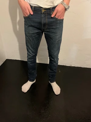 Mörkblå jeans från Lee - Säljer ett par mörkblå jeans från Lee med klassiska kontrastsömmar och femficksdesign. Jeansen har normal midja och Lee-logga på bakfickan samt läderpatch i midjan. Perfekt passform för dig som gillar en smal siluett.