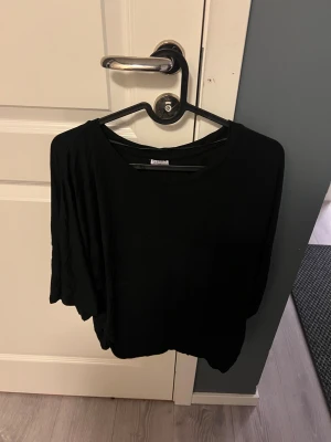 Svart loose topp från Divided - En svart, loose topp från Divided med rund hals och korta ärmar. Enkel och stilren design som funkar till många olika looks. Mjuk och lätt i materialet, perfekt för dig som gillar en avslappnad vibe.