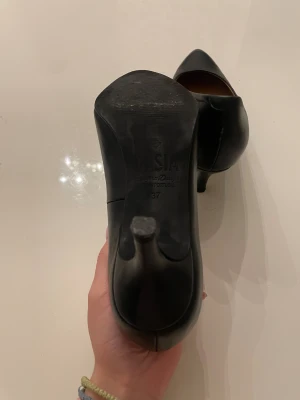 Svarta pumps från Dasia, storlek 37 - Snygga svarta pumps från Dasia i storlek 37. Skorna har spetsig tå och låg klack, tillverkade i skinn med en klassisk och stilren look. Perfekta för dig som gillar eleganta och tidlösa skor med en feminin touch. Köpta för 900kr på scorett och bara använda en natt då jag hade bal, säljer då jag ej använder klackar. Pris kan diskuteras vid snabb affär!💞