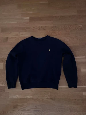 Mörkblå sweatshirt från Polo Ralph Lauren - Snygg mörkblå sweatshirt från Polo Ralph Lauren i storlek S. Men sitter som storlek xs. Klassisk design med rund hals och det ikoniska broderade logot på bröstet i gult. Tröjan har långa ärmar och är tillverkad i mjuk bomull för skön komfort. 