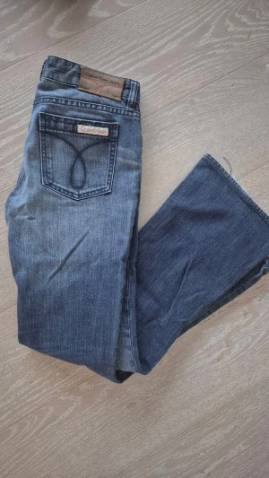 Blå bootcut jeans från Calvin Klein - Snygga blå jeans från Calvin Klein med bootcut passform. Klassisk femficksdesign, tydlig wash och logga på bakfickan. Jeansen är tillverkade i bomull och har en cool tvättad look som ger en avslappnad vibe.