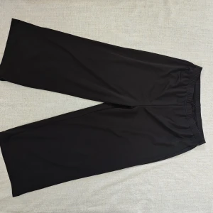 Svarta wide byxor i polyester XXL - Svarta byxor med breda ben och resår i midjan. Tillverkade i mjuk och stretchig polyesterblandning med 5% spandex för extra komfort. Perfekta för en avslappnad och trendig look.