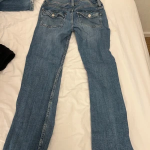 Blå jeans med ficklock och knappar - Säljer ett par klassiska blå jeans med raka ben och snygga ficklock med knappar bak. Från ginatricot