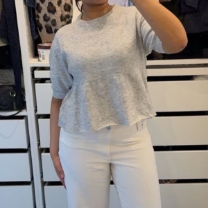 Grå loose topp med volangkant - Säljer en ljusgrå topp med lös passform och volangkant nedtill. Toppen har rund halsringning och halvlånga ärmar, perfekt för en chill och avslappnad stil. Mjuk och skön, passar till både jeans och kjol.