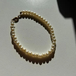 Pärlarmband med guldfärgat spänne - Ett klassiskt armband med vita pärlor i rund form och ett guldfärgat spänne. Perfekt för dig som gillar stilrena och tidlösa accessoarer. Pärlorna är jämnt placerade och ger en elegant look.