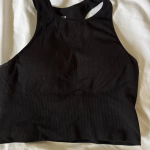Svart ribbad linnetopp med brottarrygg - Säljer en svart ribbad linnetopp från H&M med brottarrygg och rundad cut-out i ryggen. Toppen är ärmlös och har en tight passform, perfekt för träning eller chill dagar. Materialet är mjukt och stretchigt för extra komfort.