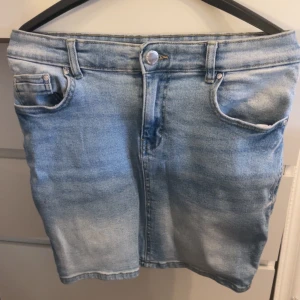 Ljusblå jeanskjol med fickor - Snygg ljusblå jeanskjol med klassisk femficksdesign och knapp framtill. Kjolen har en rak passform och är i kort modell, perfekt för en avslappnad stil. Tidlös denim som är lätt att matcha med olika toppar.