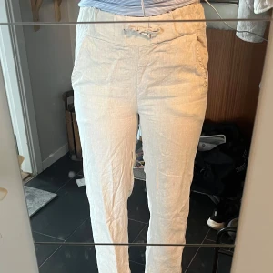 Beiga linnebyxor med dragsko - Säljer ett par beiga linnebyxor med avslappnad passform och dragsko i midjan. Byxorna har raka ben och sidofickor, perfekta för en chill och stilren look. Materialet är linne som ger en skön och luftig känsla.