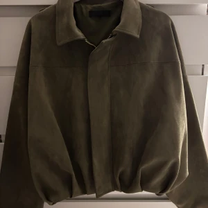 Olivgrön mockajacka med dragkedja - Säljer en olivgrön mockajacka med klassisk krage och dold dragkedja framtill. Jackan har en loose passform och långa ärmar, perfekt för dig som gillar en stilren och enkel look. Materialet är mjukt och ger en lyxig känsla.