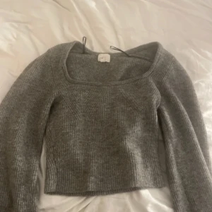 Grå ribbad croppad stickad topp - Säljer en grå croppad stickad topp från HM med fyrkantig ringning och långa ärmar. Tröjan är ribbstickad och har en mjuk, mysig känsla. Perfekt att styla med höga jeans eller kjol.