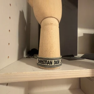 Christian Dior J'adior armband - Snyggt vävt armband från Christian Dior med texten 'CHRISTIAN DIOR J'ADIOR' i svart på vit botten. Armbandet har justerbara tofsar i ändarna och en cool, casual vibe. Perfekt accessoar för att lyfta din outfit med en touch av lyx. Kan ej garantera äkthet då jag inte har kvitto men i mina ögon så ser armbandet väldigt bra ut och är ganska säkert på att det är äkta därav priset