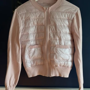 Ljusrosa quiltad kofta från Gina Tricot - Supersöt ljusrosa kofta från Gina Tricot med quiltad framsida och två fickor. Dragkedja framtill och ribbade muddar. Ärmar och baksida i mjuk stickad bomullsmix. Perfekt för lager-på-lager under kyliga dagar.