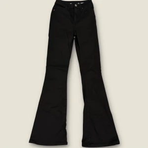 Svarta bootcut jeans med hög midja - Snygga svarta jeans med bootcut-ben och hög midja. Klassisk femficksmodell med knapp och dragkedja framtill. Perfekta för dig som gillar en retroinspirerad look med utsvängda ben. Tillverkade i mjukt och stretchigt bomullsmaterial.