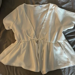 Vit omlottblus med knyt från 157 - Supersöt vit omlottblus från 157 i storlek M. Blusen har korta ärmar, v-ringning och knyt i midjan.