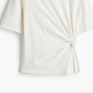 Vit omlottopp med knyt i sidan - Säljer en stilren vit topp med omlottdetalj och knyt i sidan. Toppen har korta ärmar och en rak passform som ger en clean look. Perfekt att matcha med jeans eller kjol för en fräsch stil.