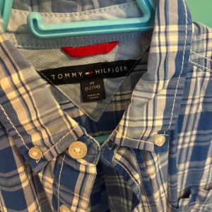 Blårutig skjorta från Tommy Hilfiger - Snygg blårutig skjorta från Tommy Hilfiger med klassisk button-down krage och bröstficka med liten logga. Skjortan har vita knappar och lång ärm, perfekt för en stilren och avslappnad look. Tillverkad i mjuk bomull för skön känsla hela dagen.