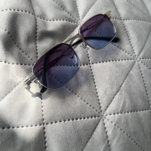 Silvriga retro solglasögon lila-blå - Snygga solglasögon med rektangulära linser i lila-blå toning och silvriga metallbågar. Tidlös retrostil med tunna skalmar och svarta detaljer vid öronen. Perfekta för dig som vill sticka ut med en cool vibe.