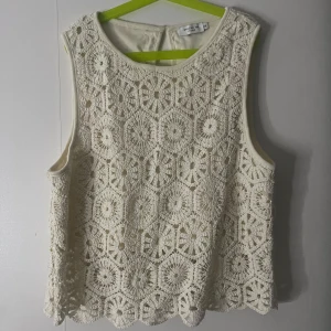Vit spetsblus från Stockholm Studio - Superfin vit blus från Stockholm Studio med vackert virkat spetsmönster i blommig stil. Ärmlös modell med rund halsringning och fodrad insida. Perfekt för dig som gillar romantiska och detaljerade plagg.
