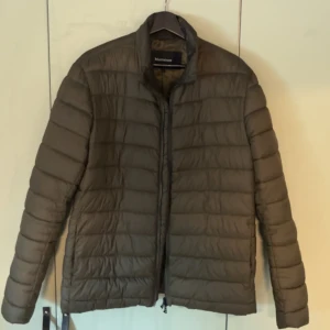 Olivgrön pufferjacka från Matinique - Säljer en olivgrön pufferjacka från Matinique med diskret logomärke på bröstet. Jackan har horisontella sömmar, dragkedja framtill och en stilren, enkel design. Perfekt för kyliga dagar och lätt att matcha med olika outfits.