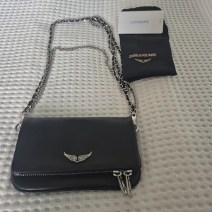 Zadig & Voltaire: Rock Nano väska – sparsamt använd - Säljer min Rock Nano-väska från Zadig & Voltaire med tillhörande dustbag. Väskan är köpt på Zoovillage och har använts vid ett fåtal tillfällen – i fint skick.  Jag har varit supernöj, men den kommer tyvärr inte längre till användning. Hoppas den får ett nytt hem där den uppskattas lika mycket!  Mått: ca 18 x 11 cm