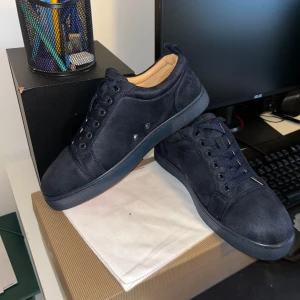 Mörkblå Christian Louboutin sneakers - Säljer ett par mörkblå sneakers från Christian Louboutin i mocka med klassisk röd sula och snygg snörning. Skorna har rund tå och diskret broderad logga på hälen. Perfekta för dig som vill sticka ut med exklusiv stil och detaljer.