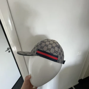 Gucci keps  - Snygg keps från Gucci i beige och marinblått med klassiskt GG-monogram över hela kepsen. Har en röd och marinblå rand på sidan och justerbar rem baktill. Tillverkad i bomullscanvas med detaljer i skinn. Perfekt för dig som vill sticka ut med en lyxig accessoar. Pris kan diskuteras och skriv vid frågor (: