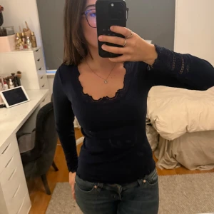 Mörkblå topp med spets från Rosemunde - Supersnygg mörkblå långärmad topp från Rosemunde med vacker spetskant vid ringningen och ärmsluten. Gjord i en lyxig mix av silke och bomull som känns riktigt skön mot huden. Figurnära passform och ribbad struktur för en stilren look.