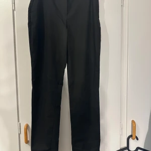 Svarta kostymbyxor från H&M - Svarta kostymbyxor från H&M med klassisk rak passform och dragkedja framtill. Byxorna har diskreta fickor och är tillverkade i ett mjukt material som känns bekvämt hela dagen. Perfekta för en clean och stilren look.