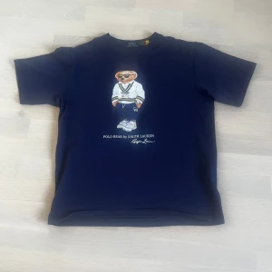Mörkblå Polo Bear t-shirt Ralph Lauren - Snygg mörkblå t-shirt från Ralph Lauren med Polo Bear-tryck på bröstet. Storlek m passar bra kan få bild på om det efterfrågas 