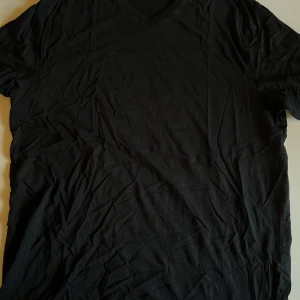 Svart t-shirt med v-ringning Dressmann - Svart t-shirt från Dressmann i storlek 2XL. Klassisk modell med v-ringad hals och korta ärmar. Tillverkad i Fairtrade-märkt bomull, perfekt för en clean och enkel stil.