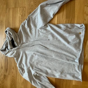 Grå hoodie från Pernilla Wahlgren XS - Säljer en stilren ljusgrå hoodie från Pernilla Wahlgren i storlek XS. Tröjan har huva med snörning och långa ärmar. Perfekt för chill dagar och enkel att matcha med jeans eller leggings.