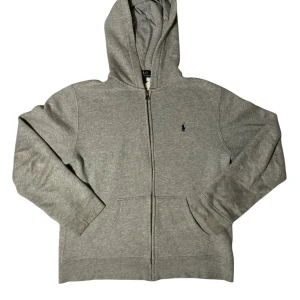 Grå hoodie från Polo Ralph Lauren - Klassisk grå hoodie från Polo Ralph Lauren med dragkedja framtill, broderad logga på bröstet och känguruficka. Mjuk bomullsblandning och huva gör den perfekt för chill dagar. Enkel och stilren design som funkar till allt. Tveka inte på att komma med frågor eller prisförslag ⬜️🟦