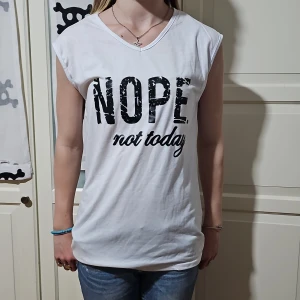 Vit ärmlös t-shirt med tryck - Vit ärmlös t-shirt i bomull med svart texttryck 'NOPE not today' på framsidan. Modellen är loose fit med v-ringning och mjukt material, perfekt för en chill och avslappnad stil.